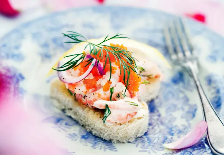 En läcker toast Skagen med räkor, rom, dill och rödlök på en blåvit tallrik.
