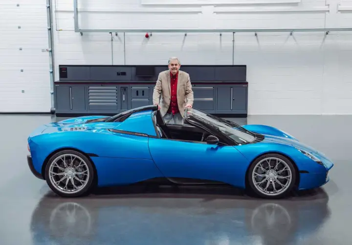 Gordon Murray präsentiert stolz seinen neuen Gordon Murray T.33, einen leuchtend blauen Supersportwagen in einer Werkstatt.
