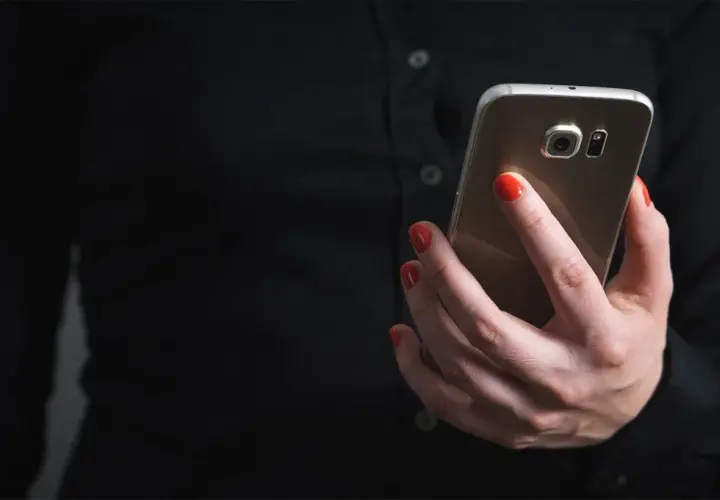Dłoń z czerwonymi paznokciami trzyma telefon, szukając informacji, jak zablokować SMS premium.