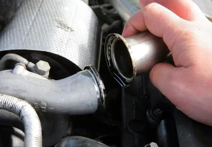 Dłoń trzymająca metalową rurkę z widocznymi śladami oleju, część układu dolotowego turbiny auto.