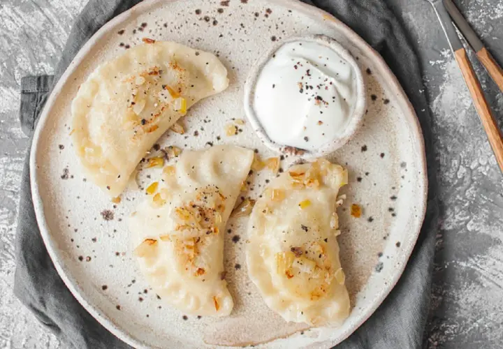 Jak odgrzać pierogi w mikrofali? Na talerzu ułożone pierogi z cebulką i śmietaną, gotowe do szybkiego podgrzania.