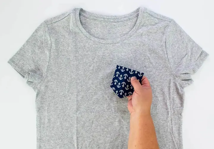 A hand holds a navy fabric with white anchors, demonstrating how to sew front pockets on pants.
