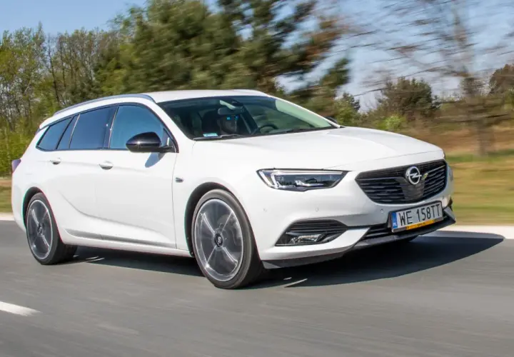 Białe kombi Opel Insignia 2.0 CDTI pędzi po drodze, za kierownicą mężczyzna w okularach przeciwsłonecznych.