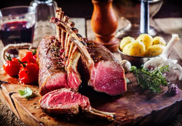 Un succulent carré d'agneau rôti, accompagné de tomates cerises, de pommes de terre et d'une touche d'herbes fraîches.