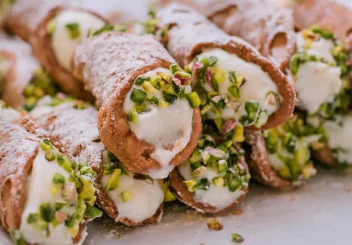 Słodkie rurki wypełnione kremowym serek ricotta, posypane cukrem pudrem i pistacjami. Pyszna włoska przekąska.