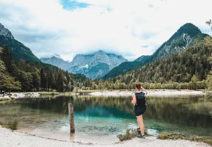 Frau mit Rucksack genießt den Blick auf einen türkisfarbenen See und die Berge. Perfekter Ort zum Wandern in Slowenien.
