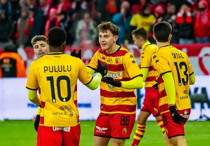 Piłkarze Jagiellonii Białystok świętują. Na boisku w meczu przeciwko Górnikowi Zabrze, zawodnicy w żółto-czerwonych strojach cieszą się z sukcesu.
