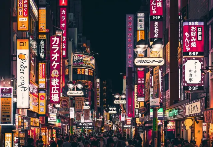 Nocna ulica Tokio z neonowymi szyldami i tłumem ludzi.