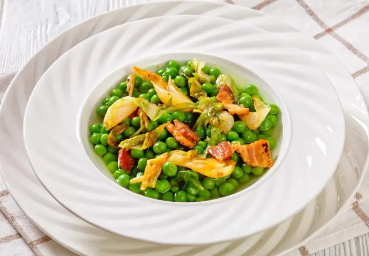Un plat de petit pois à la française, garni de lardons croustillants et de légumes tendres, servi dans une assiette blanche élégante.