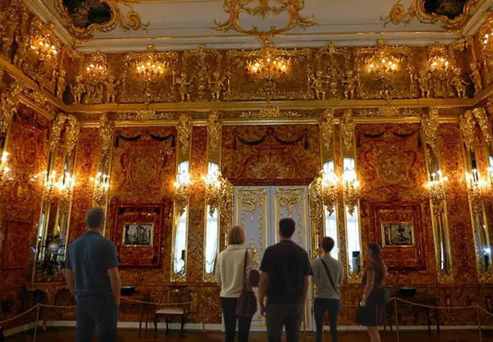 Zachwycająca bursztynowa komnata, gdzie złote zdobienia i światło tworzą magiczną atmosferę. Zwiedzający podziwiają jej piękno.