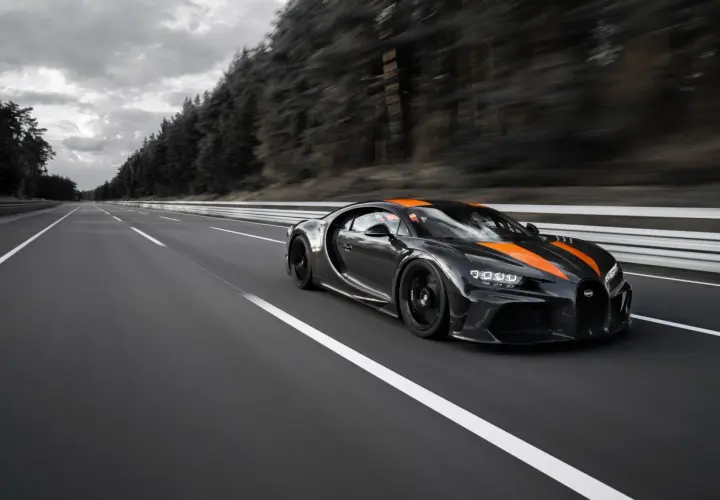 Czarny Bugatti Chiron Super Sport z pomarańczowymi pasami pędzi po pustej autostradzie.