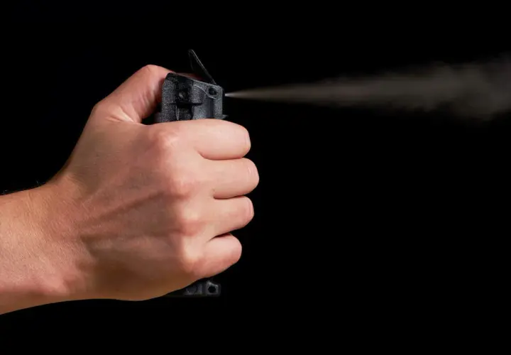 Main d'une personne actionnant une bombe lacrymogène, le jet de gaz se dispersant dans l'air. La loi encadre l'usage de ce type de défense.