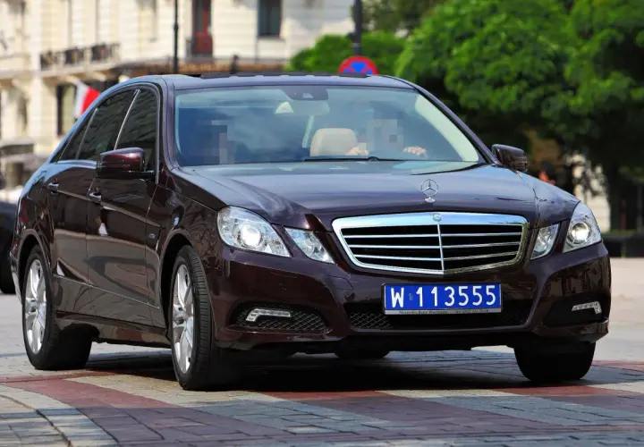 Ciemnobrązowy Mercedes z niebieską tablicą rejestracyjną W 113555, typową dla pojazdów dyplomatycznych w Polsce.