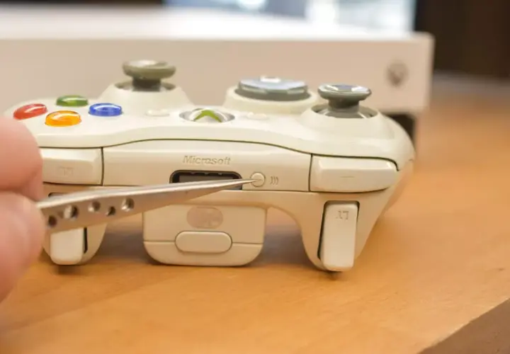Pęseta zbliża się do przycisku synchronizacji na białym padzie Xbox. Dowiedz się, jak podłączyć drugiego pada Xbox.