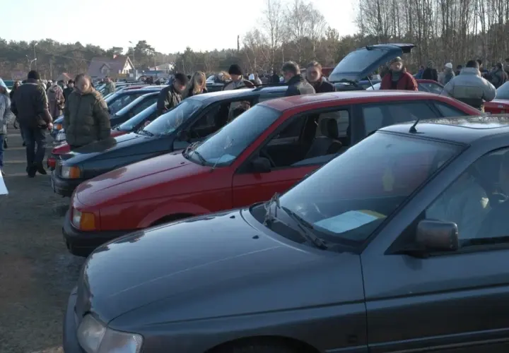 Rząd samochodów na placu, ludzie oglądają auta.