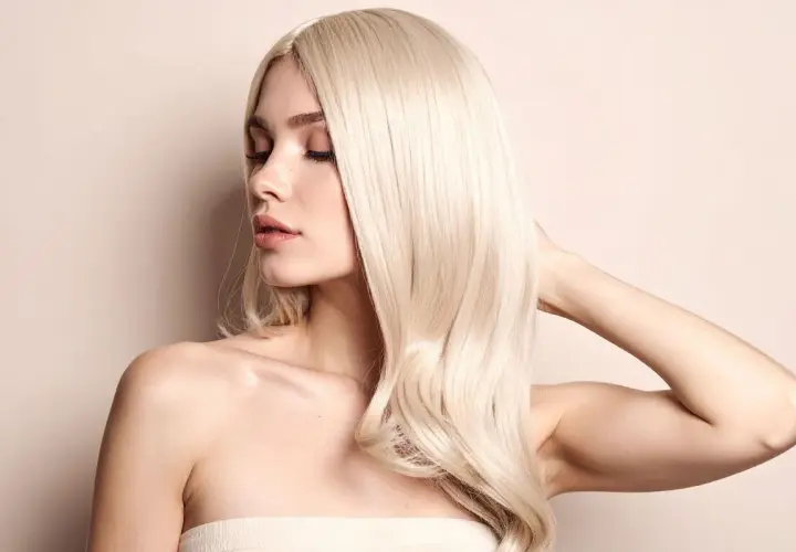 Kobieta z burzą włosów w odcieniu platynowy blond, z zamkniętymi oczami i delikatnym uśmiechem.