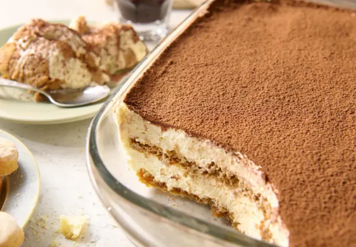 Najprostsze tiramisu w szklanej formie, posypane kakao. Na talerzyku porcja deseru i łyżeczka.