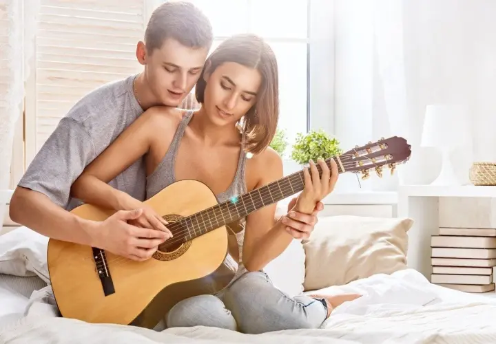 Para tworzy najpiękniejsze melodie o miłości, grając razem na gitarze w przytulnym pokoju.