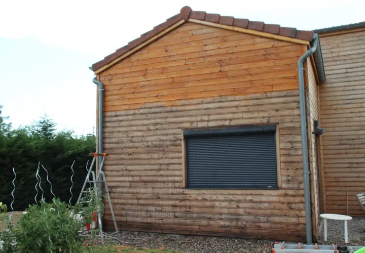 Échelle près d'un mur en bois, suggérant un entretien du bardage bois. Le bois est plus clair en haut, plus foncé en bas.