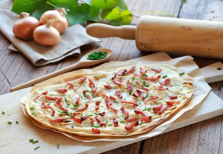 Flammekueche prête à être dégustée, avec ses oignons, lardons et ciboulette. Une recette simple et savoureuse.