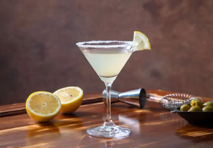Elegancki drink Martini Bianco z cytryną i solą na kieliszku, obok połówki cytryny i oliwek.