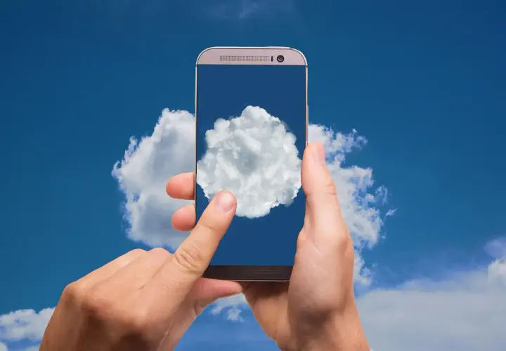 Dłonie trzymają telefon, na którego ekranie widać chmurę. To symbol tego, gdzie jest chmura w telefonie – w chmurze danych.