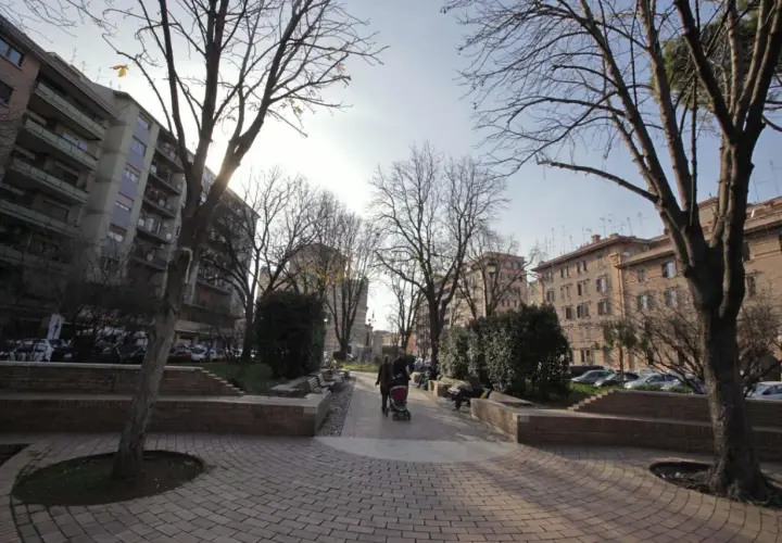 Passeggiata in un parco urbano, ideale per capire come arrivare a Testaccio da Termini. Alberi spogli, palazzi e persone con un passeggino.