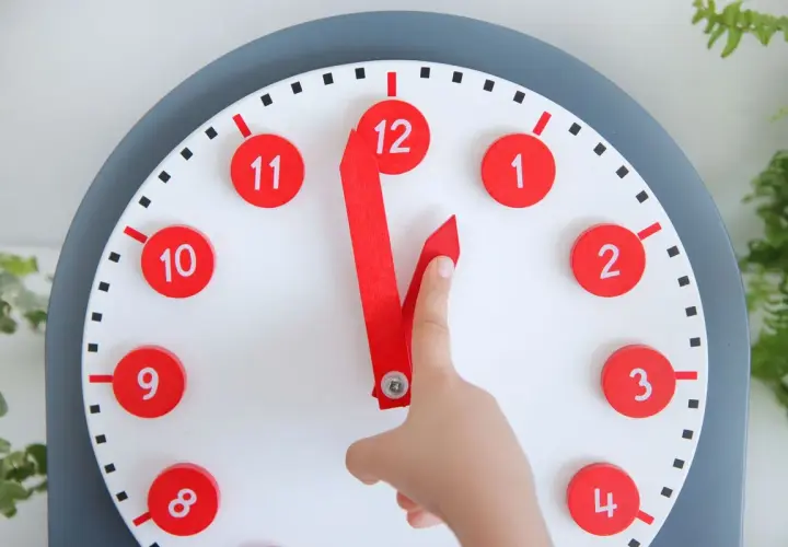 Un niño aprende las horas con un reloj didáctico. Las manecillas rojas apuntan a las 12 y las 11.