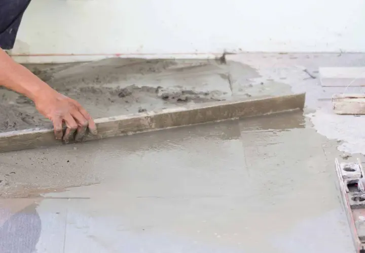 Ręka pracownika wyrównuje świeżą wylewkę betonową. Zastanawiasz się, ile waży wylewka betonowa?