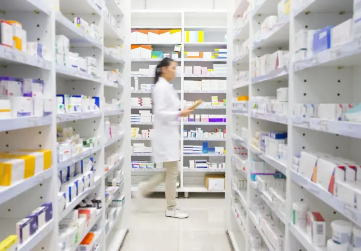 Farmaceutka w białym fartuchu przeszukuje półki apteki, szukając leku milurit 300.