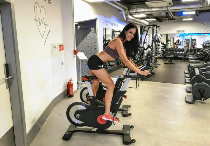 Kobieta ćwiczy na rowerze stacjonarnym w siłowni. To świetny sposób na poprawę kondycji, czy to cardio, czy kardio – ważne, by się ruszać!