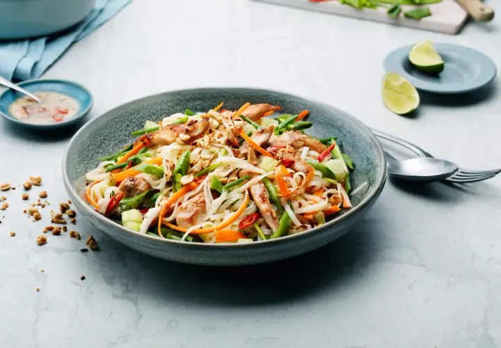 En läcker asiatisk nudelsallad med kyckling, grönsaker och jordnötter. Serveras med en dressing och limeklyftor.