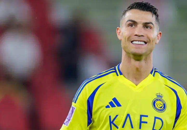 Uśmiechnięty Cristiano Ronaldo w żółtej koszulce z niebieskimi pasami, grający w klubie Al Nassr.