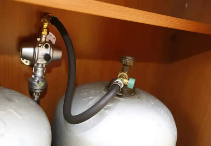 Connexion pour remplir bouteille de gaz au GPL. Tuyau noir relié à une valve verte sur la bouteille.