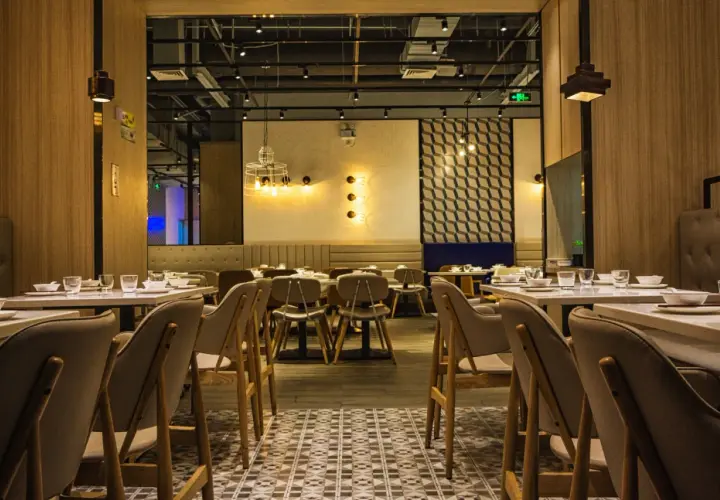 Przytulne wnętrze restauracji z drewnianymi panelami i stylowym oświetleniem. Stoliki nakryte, gotowe na gości.