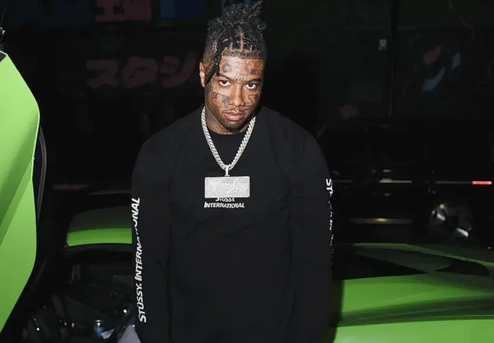 Raper z tatuażami na twarzy, znany jako blueface, pozuje obok jaskrawozielonego samochodu sportowego.