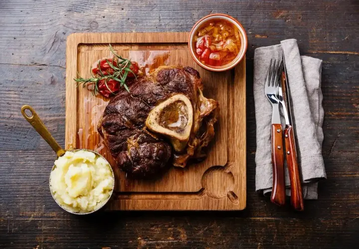 Wołowe ossobuco z puree ziemniaczanym, sosem i gałązką rozmarynu na desce.
