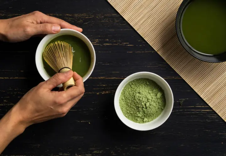 Hände bereiten Matcha zu. Pulver und fertiger Tee auf dunklem Holz. Eine positive matcha tee abnehmen erfahrung beginnt hier.