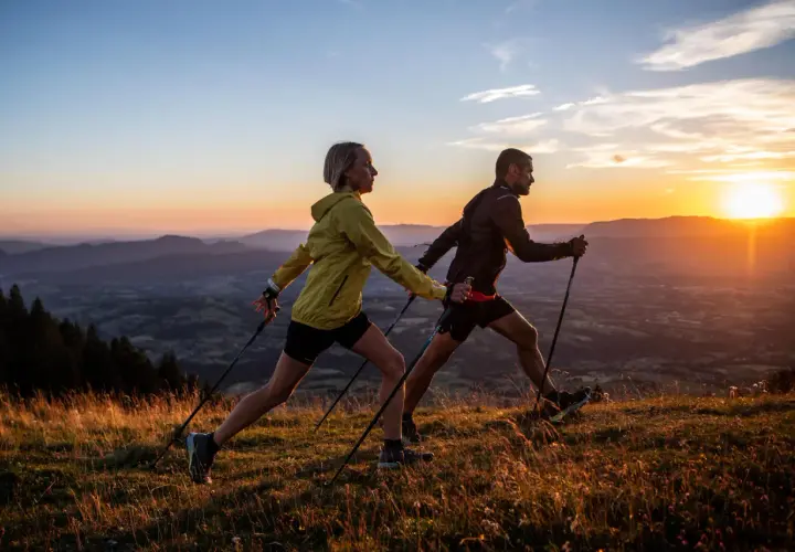 Para uprawiająca nordic walking na tle zachodzącego słońca nad górami.