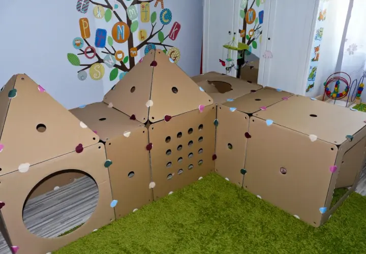 Kreatywne zabawki z kartonu diy tworzą domek do zabawy. Kolorowe serduszka zdobią kartonowe ściany, a otwory zapraszają do eksploracji.