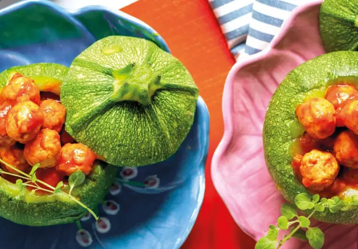 Zucchine tonde ripiene di polpettine in salsa, servite in ciotole colorate. Un piatto invitante e gustoso.