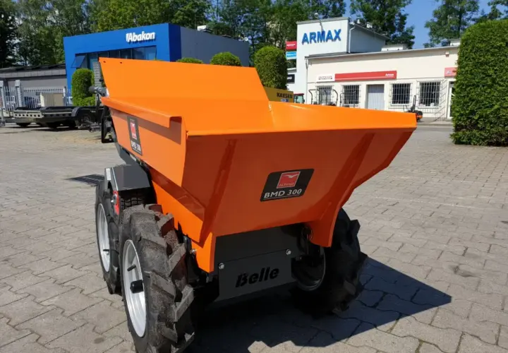 Pomarańczowe, małe wozidła budowlane stoją na placu przed budynkami.