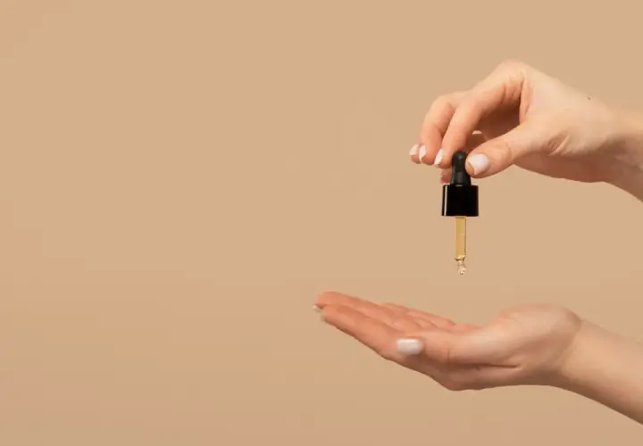 Una mano sostiene un gotero con aceite de jojoba para el pelo, listo para aplicarlo en la otra mano.