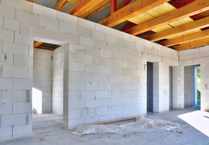 Budowa domu z białych bloczków z betonu komórkowego, widoczne drewniane belki stropowe.