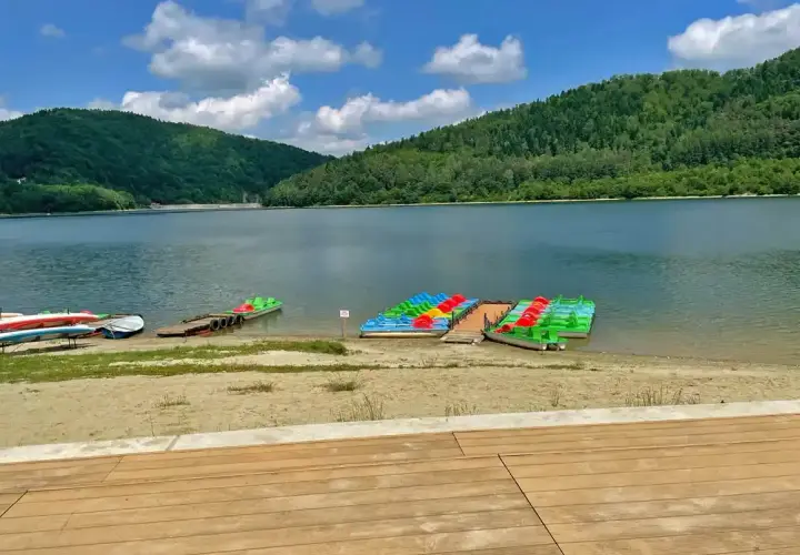 Kolorowe rowery wodne i kajaki czekają na plaży nad górskim jeziorem.