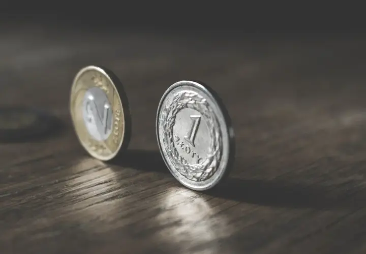 Dwie polskie monety, 1 złoty i 2 złote, na drewnianym blacie. Marzenie o pensji 6500 brutto.