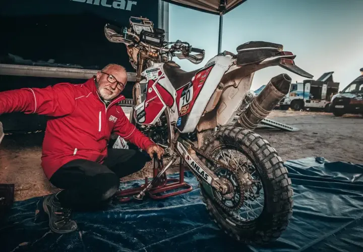 Uomo in giacca rossa vicino a moto da cross sporca, pronto a capire come pulire il motore dopo una gara.