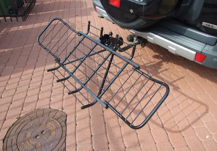 Czarny, metalowy uchwyt do przewozu motocykla na hak, gotowy do montażu przy samochodzie.
