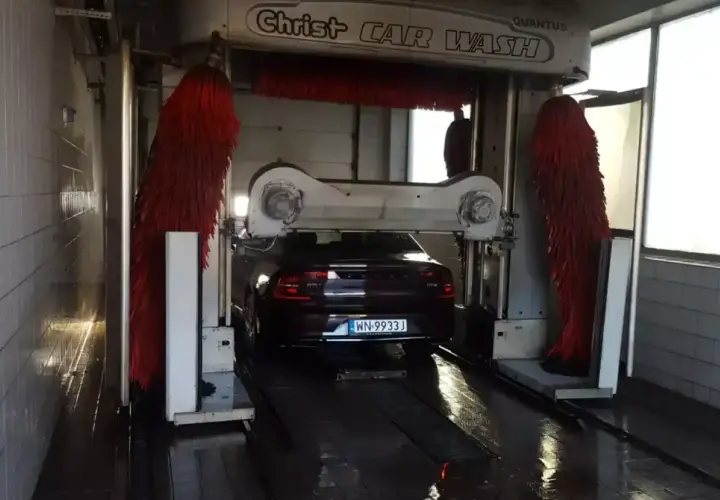 Ciemny Volvo czeka na mycie auta w automatycznej myjni. Czerwone szczotki są gotowe do pracy.