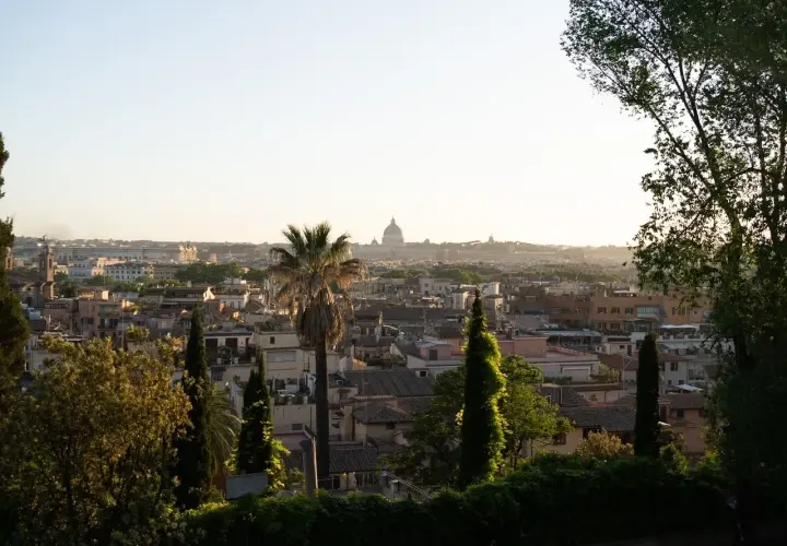 Panoramic view of Rome with St. Peter's Basilica dome in the distance, framed by trees and greenery.